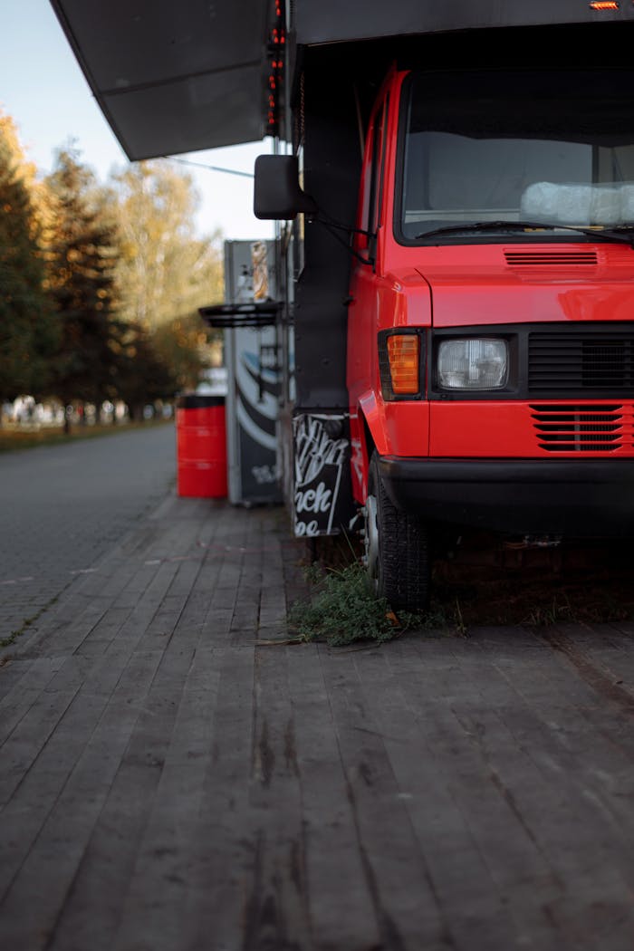 about-us A vibrant red food truck parked on a tree-lined street during autumn.